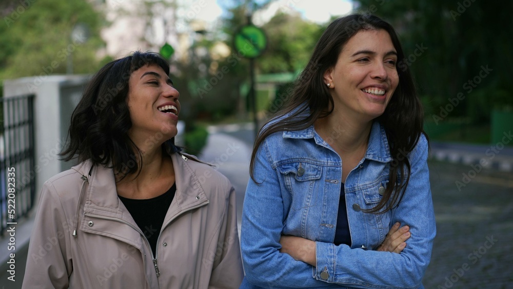 Two happy young women girlfriends walking outside laughing and smiling together on street Two happy young women girlfriends walking outside laughing and smiling together on street