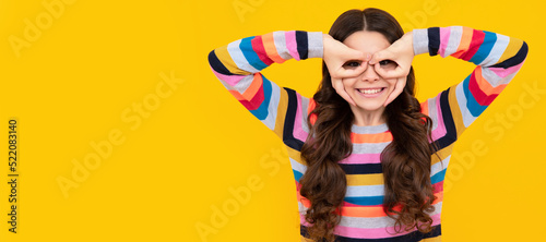 Beautiful teenager child girl look finger specs okey symbol silly shapes figures isolated on yellow background. Child face, horizontal poster, teenager girl isolated portrait, banner with copy space.