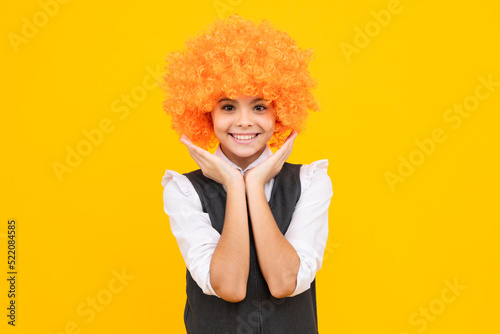 Funny kid with curly hair wig. Cute little girl with fancy hair. Child wearing bright redhead clown hair wig. Happy girl face, positive and smiling emotions.