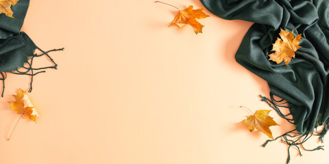Autumn composition.Trendy green scarf and yellow leaves on isolated beige background. Autumn, fall concept. Flat lay, top view, copy space