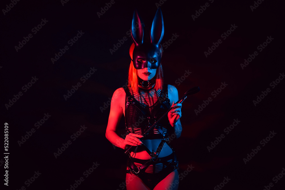 sexy mistress girl in beautiful underwear and a hare mask holds a leather flogger whip for BDSM sex with domination and submission - obrazy, fototapety, plakaty 
