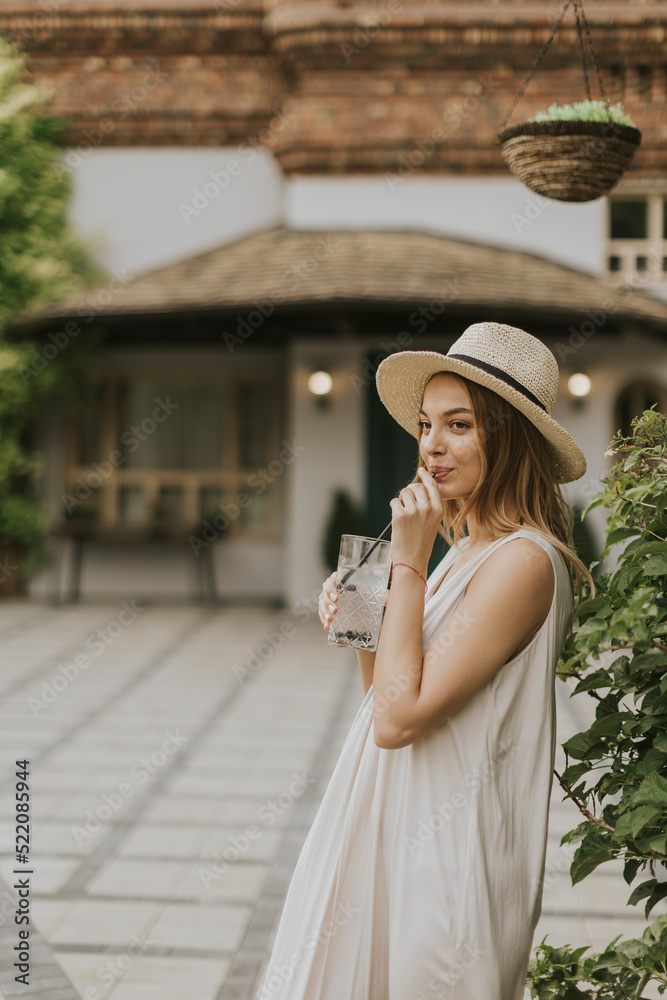 Young woman with hat drinking cold lemonade in the resort garden