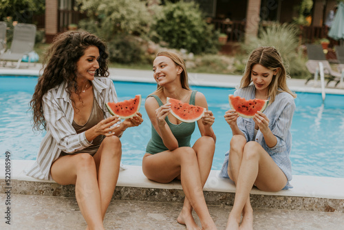 Young woman sitting on by the swimming pool and eating watermelon in the house backyard