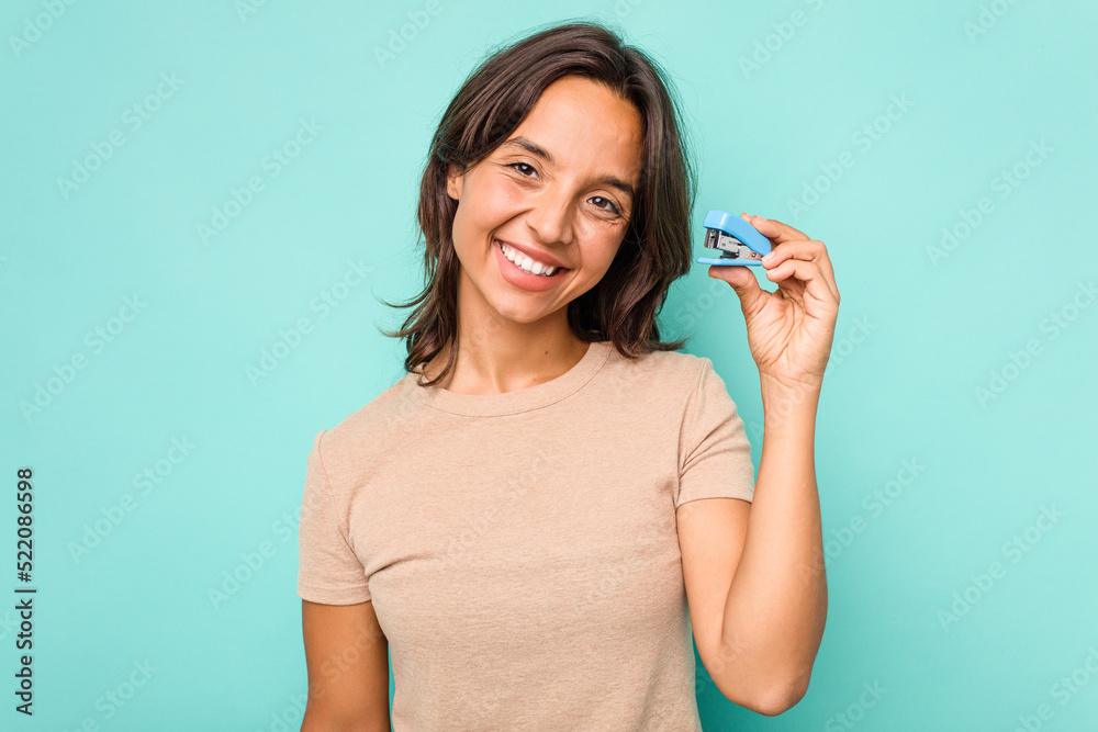 Young hispanic woman holding stapler isolated on blue background happy, smiling and cheerful. Young hispanic woman holding stapler isolated on blue background happy, smiling and cheerful.