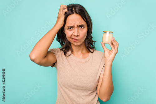 Young hispanic woman holding yogurt isolated on blue background being shocked, she has remembered important meeting.