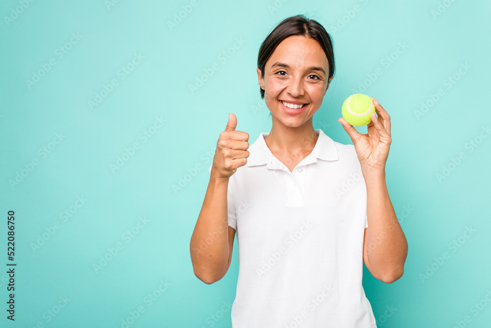 Young hispanic physiotherapy holding a tennis ball isolated on blue background smiling and raising thumb up Young hispanic physiotherapy holding a tennis ball isolated on blue background smiling and raising thumb up
