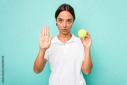Young hispanic physiotherapy holding a tennis ball isolated on blue background standing with outstretched hand showing stop sign, preventing you. © Asier