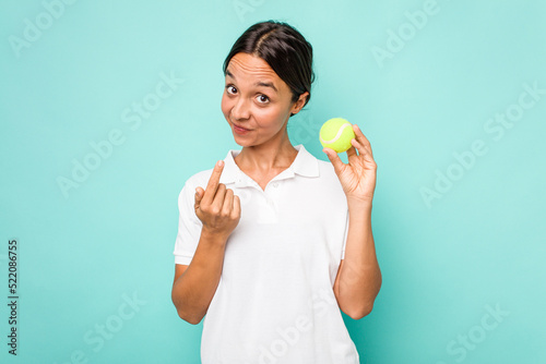 Young hispanic physiotherapy holding a tennis ball isolated on blue background pointing with finger at you as if inviting come closer. © Asier
