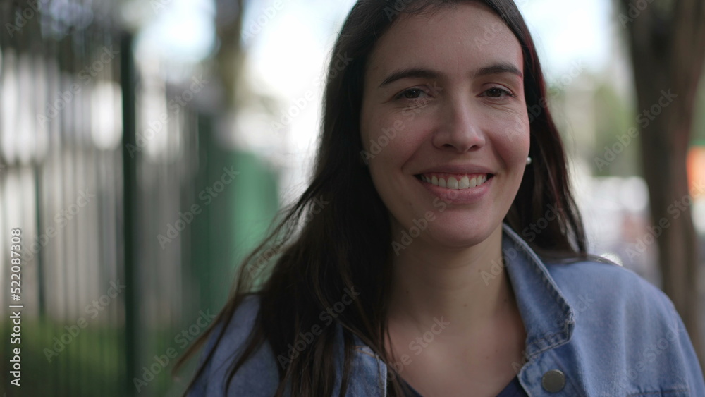 Confident happy woman walking forward in street looking at camera. Person in 30s portrait face closeup walks in sidewalk Confident happy woman walking forward in street looking at camera. Person in 30s portrait face closeup walks in sidewalk