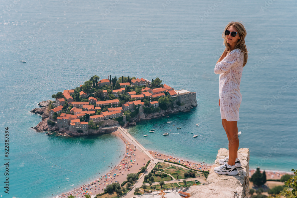 a girl poses on a mountain with a top view of the city of Sveti Stefan in Montenegro, a picturesque bay