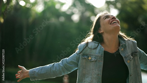 Carefree happy woman arms raised outside looking at sky feeling grateful. Person celebrating life standing in nature sunlight photo