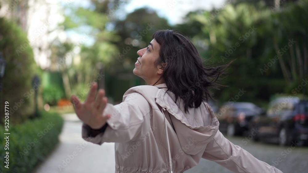 Back of carefree young woman jumping with joy in street flying in the air with arms raised pretending to fly Back of carefree young woman jumping with joy in street flying in the air with arms raised pretending to fly