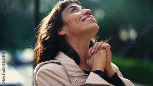 A grateful hispanic woman praying to God with hands clenched looking at sky smiling. Spiritual person having HOPE photo