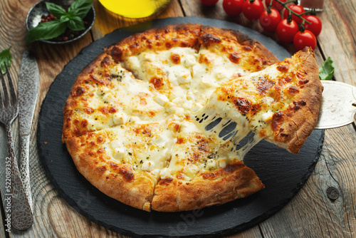 A slice of hot Italian pizza with stretching cheese. Pizza four cheeses with basil.