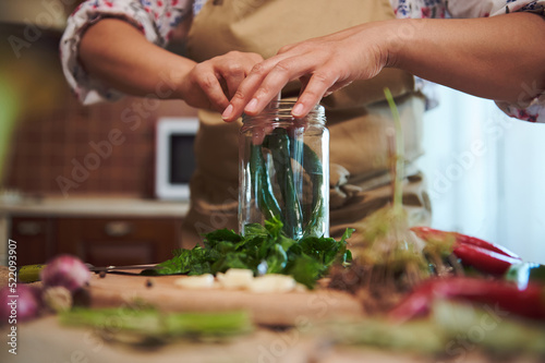 Close-up of filling sterilized glass jar with spicy chili peppers, chopped fresh dill leaves, garlic when pickling seasonal vegetables in the kitchen. Canning food and making preserves for the winter.