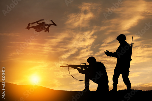 Silhouettes of soldiers are using drone and laptop computer for scouting during military operation against the backdrop of a sunset. Greeting card for Veterans Day, Memorial Day, Independence Day.
