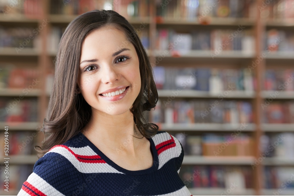 A young beautiful teenager girl smile looking at camera in university library, concept of higher education, high school excellent pupil portrait, studentship concept