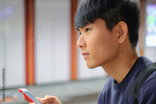 Young handsome asian man looking forward while using cellphone checking social media, surfing internet, and mobile apps at weekend at subway
