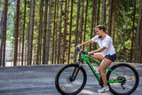 A young woman rides a bicycle in a mountainous area in the forest.
