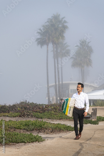 Young Japanese business professional walking with a surf board on a foggy day in San Diego California
