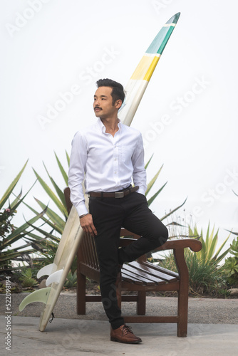 Young Japanese business professional leaning against a surf board in San Diego California
