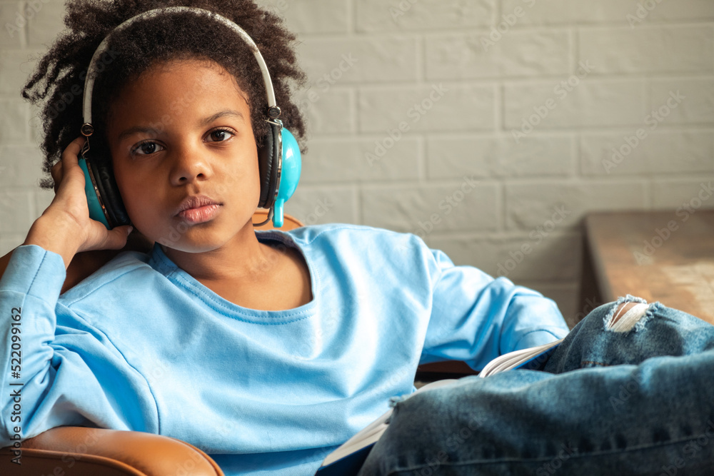 Cute African-American girl with headphones and a book in her hands is studying at home.Back to school concept.School distance education,home schooling,e-learning,diverse people. Cute African-American girl with headphones and a book in her hands is studying at home.Back to school concept.School distance education,home schooling,e-learning,diverse people.