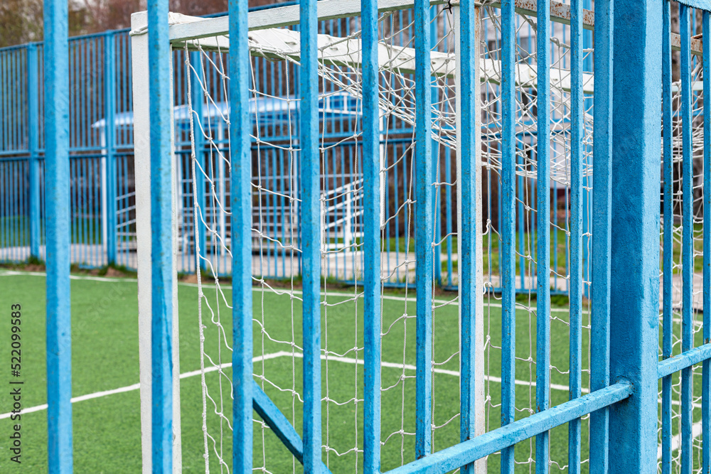 Obraz premium Football field. View of the football field with white goals through the blue fence. Sports concept, soccer field and soccer goal with grass floor.
