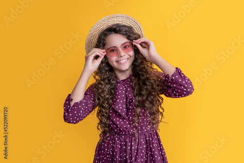 child smile in straw hat and sunglasses with long brunette curly hair on yellow background