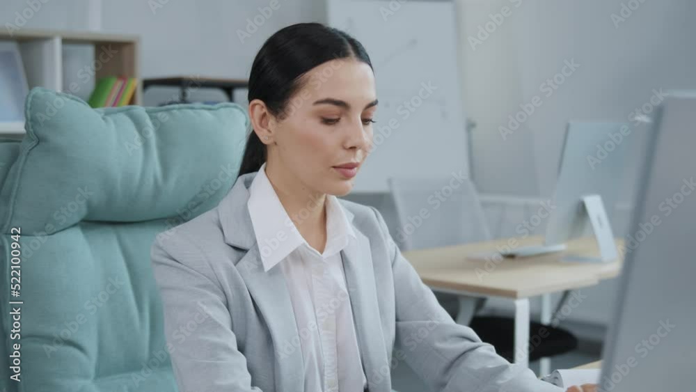 Portrait of beautiful business woman wearing elegant gray suit sitting at computer in modern comfortable office. Gorgeous brunette lady looking at camera. Daytime, work, job. Indoors Portrait of beautiful business woman wearing elegant gray suit sitting at computer in modern comfortable office. Gorgeous brunette lady looking at camera. Daytime, work, job. Indoors