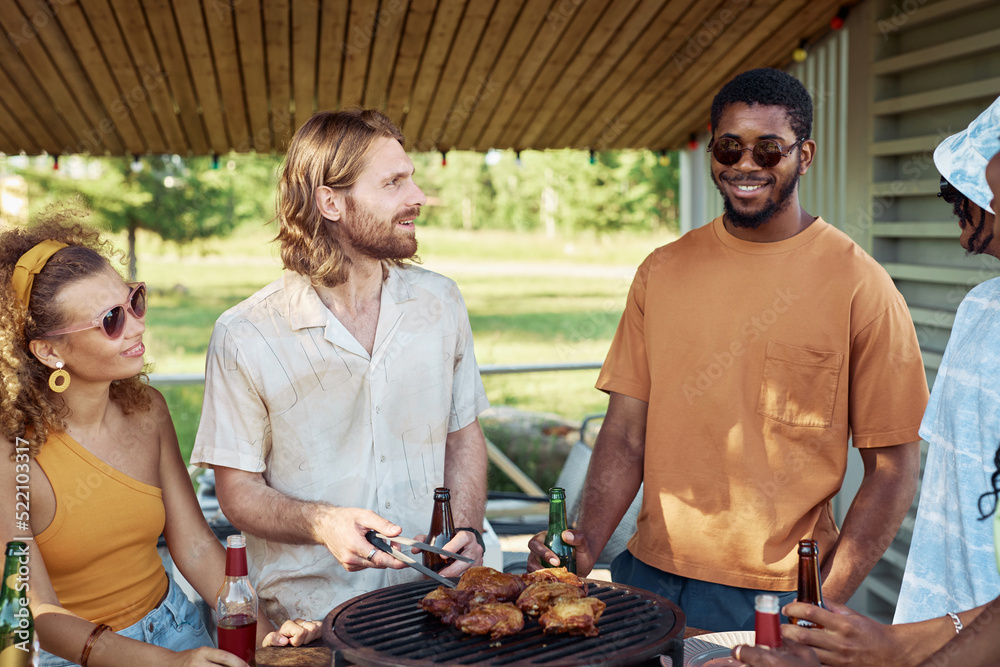Portrait of two young men grilling meat outdoors with diverse group of friends at barbeque party in Summer Portrait of two young men grilling meat outdoors with diverse group of friends at barbeque party in Summer