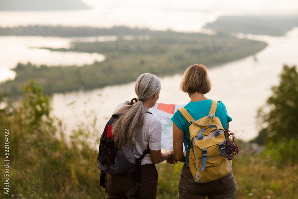 two middle aged women friends with backpacks watching the map standing on the mountain and hiking in nature and spending time together. travel tourism concept. Outdoor activities on weekends. two middle aged women friends with backpacks watching the map standing on the mountain and hiking in nature and spending time together. travel tourism concept. Outdoor activities on weekends.
