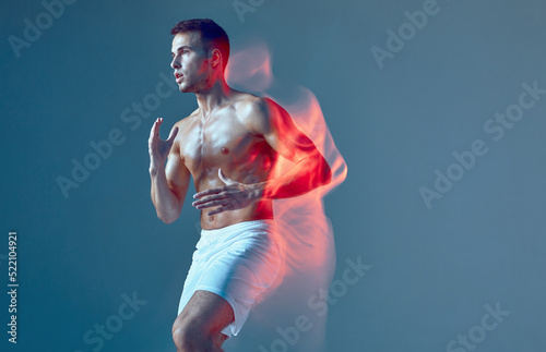 Healthy sporty male dancer at Zumba fitness training in studio. Light painting effect on blue background.