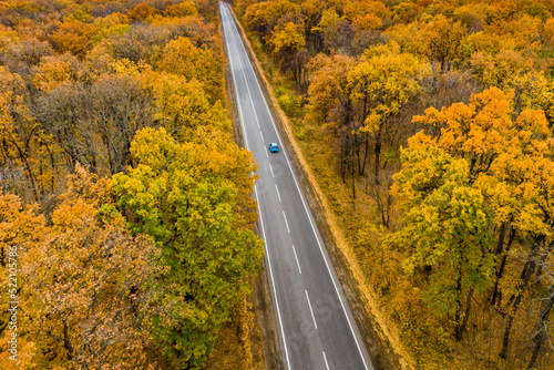 blue car driving on an asphalt road through the autumn forest. Drone photo aerial view