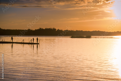 A quiet lake in the south of Sweden overlooking a wooden jetty with people in the sunset
