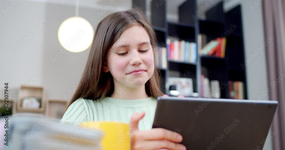 Close up of Caucasian teen girl smiling while watching something on tablet device at home. Beautiful cheerful teenager schoolgirl tapping and scrolling on computer in nice room. Inside. Close up of Caucasian teen girl smiling while watching something on tablet device at home. Beautiful cheerful teenager schoolgirl tapping and scrolling on computer in nice room. Inside.