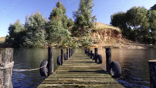 Camera moving out to the end of an old wooden footbridge that extends out onto a lake.