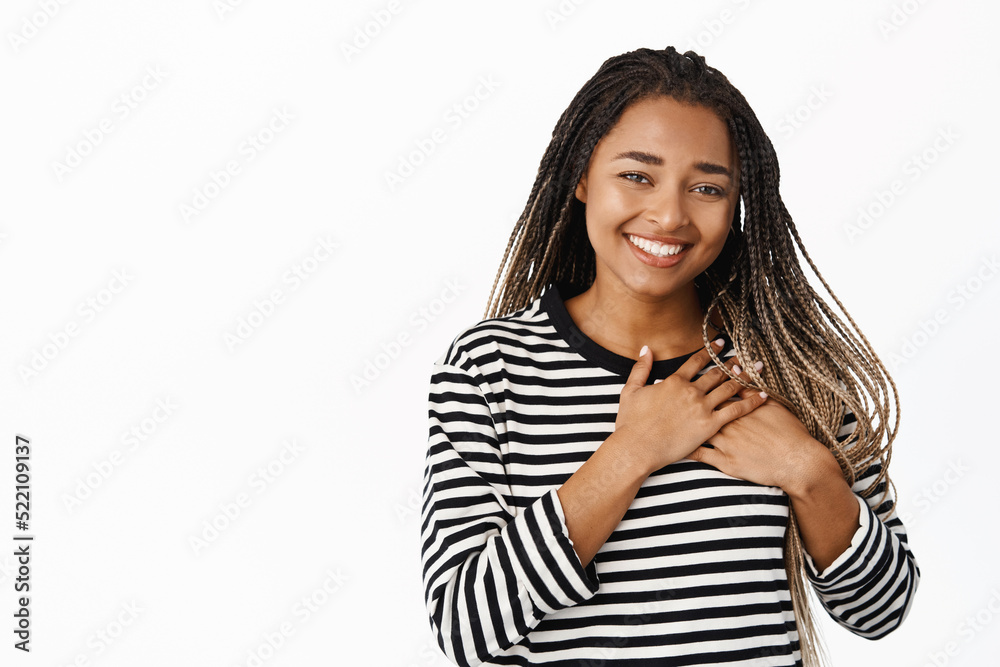 Close up portrait of black woman smiling, holding hands on heart, thank you gesture, being touched or grateful, standing over white background Close up portrait of black woman smiling, holding hands on heart, thank you gesture, being touched or grateful, standing over white background