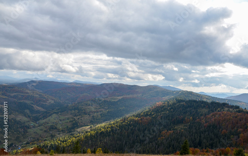 Autumn mountain landscape with hills covered picturesque and colorful forest under low clouds. Carpathian Mountains, Ukraine