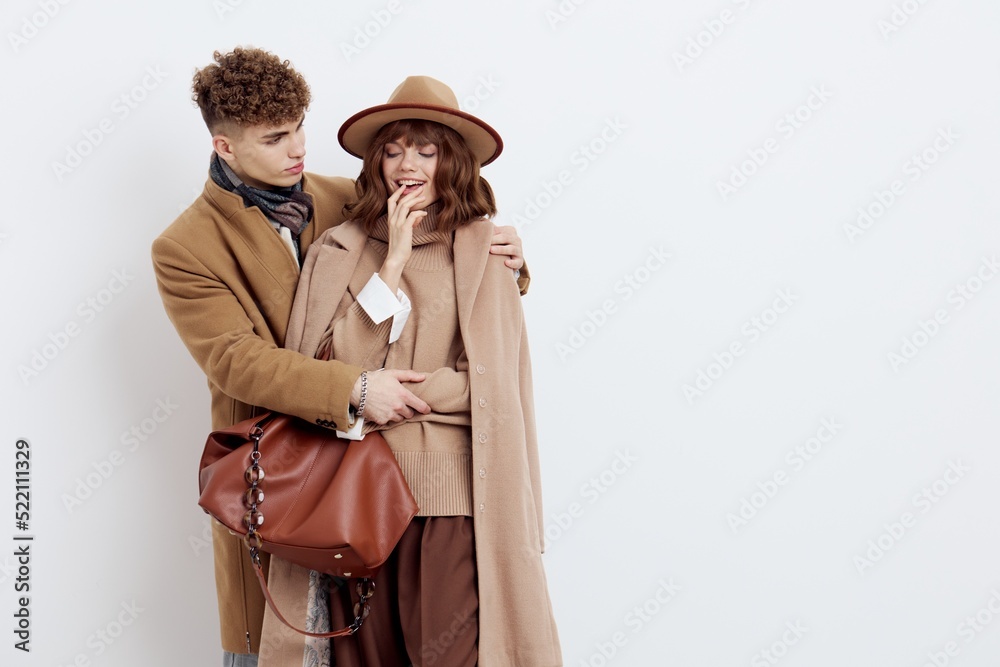 a beautiful, loving couple of a man and a woman stand on a white background in stylish autumn clothes, gently embracing and the woman joyfully holds her hand near her face a beautiful, loving couple of a man and a woman stand on a white background in stylish autumn clothes, gently embracing and the woman joyfully holds her hand near her face