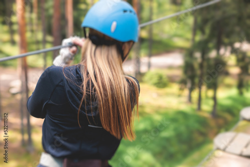 View of high ropes course, process of climbing in amusement acitivity rope park, passing obstacles and zip line on heights in climbing safety equipment gear between the trees, summer sunny day
