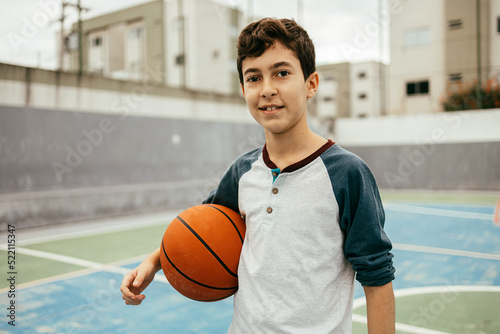 Portrait of 12 year old boy with basketball. Teenager training basketball outdoors.