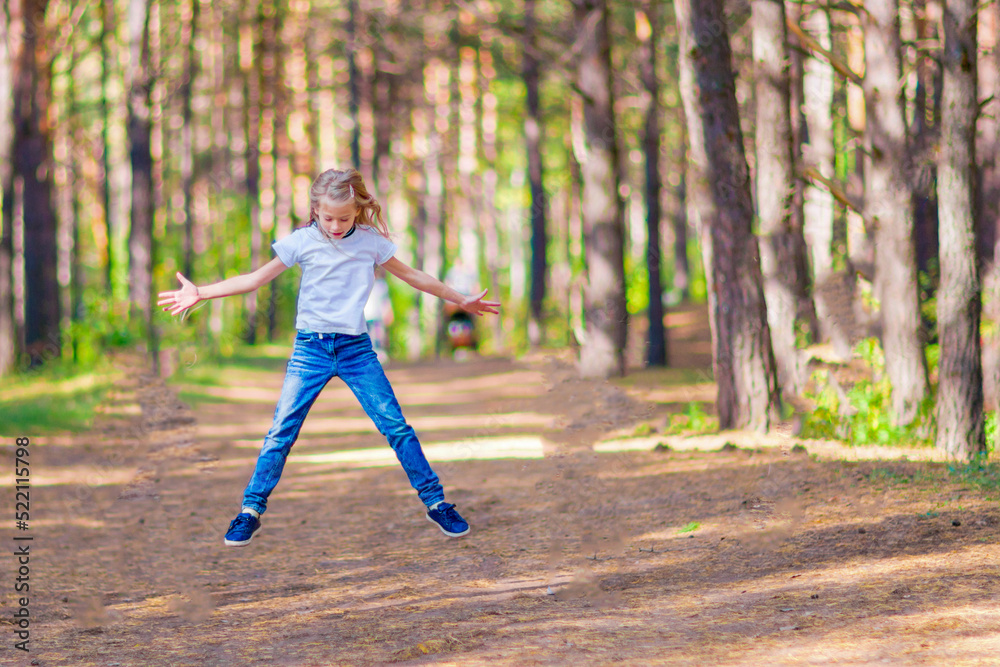 Little girl jumping outdoors in the forest. On the background of trees