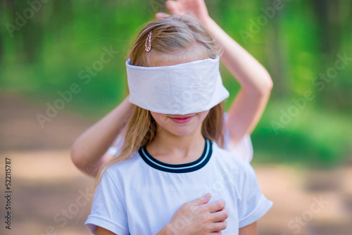 The girl is blindfolded for playing blind man's buffoonery outdoors in the forest