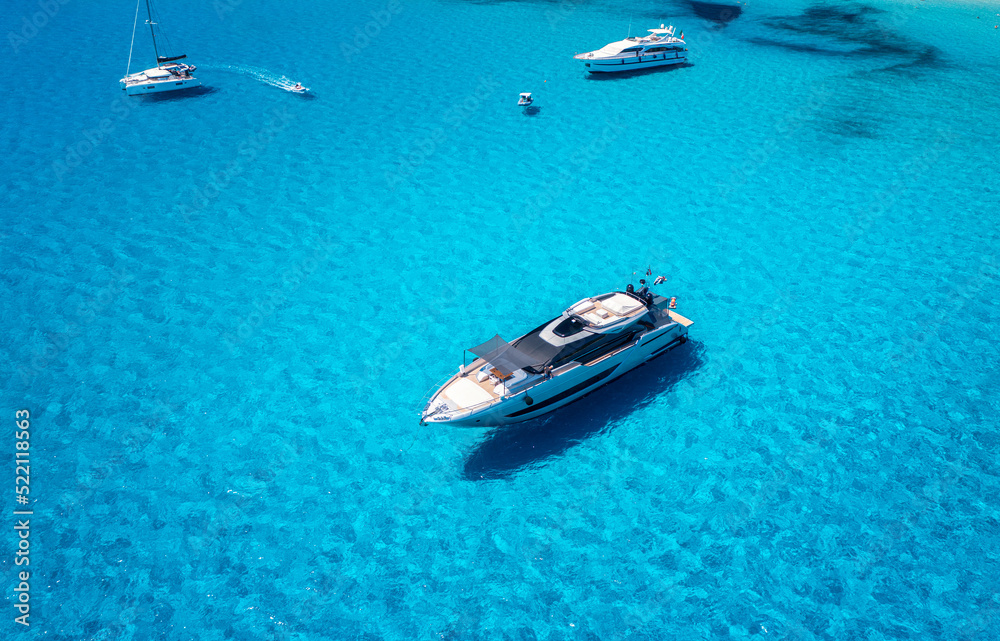 Aerial view of beautiful luxury yacht and sailboats in blue sea at sunset in summer. Sardinia island, Italy. Top view of speed boat, sea coast, transparent water. Travel. Tropical landscape. Yachting 