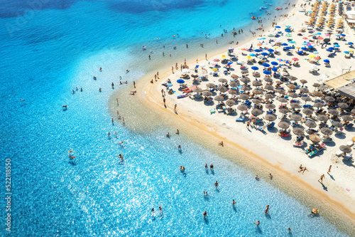 Aerial view of colorful umbrellas on sandy beach, people in blue sea at sunset in summer. Tuerredda Beach, Sardinia, Italy. Tropical landscape with turquoise water. Travel and vacation. Top view	 photo