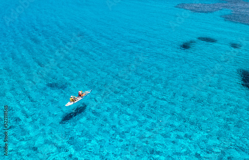 Aerial view of kayak with people in blue sea at sunset in summer. Man and woman on floating canoe in clear azure water. Sardinia island, Italy. Tropical landscape. Sup board. Active travel. Top view
