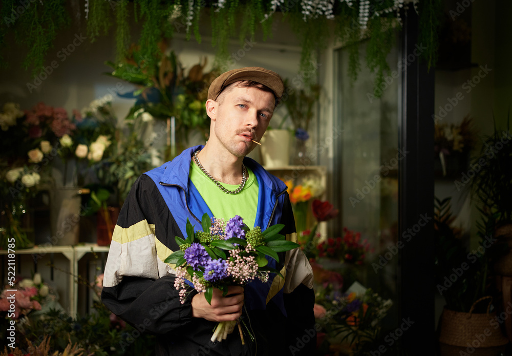 Congratulating with flowers: portrait of man in peaked cap and tracksuit holding spring flower bouquet standing indoor in flower store. Love, dating or romance concept. High quality photo
