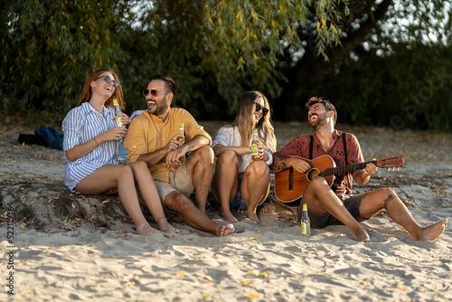 group of friends having fun on the beach playing guitar singing