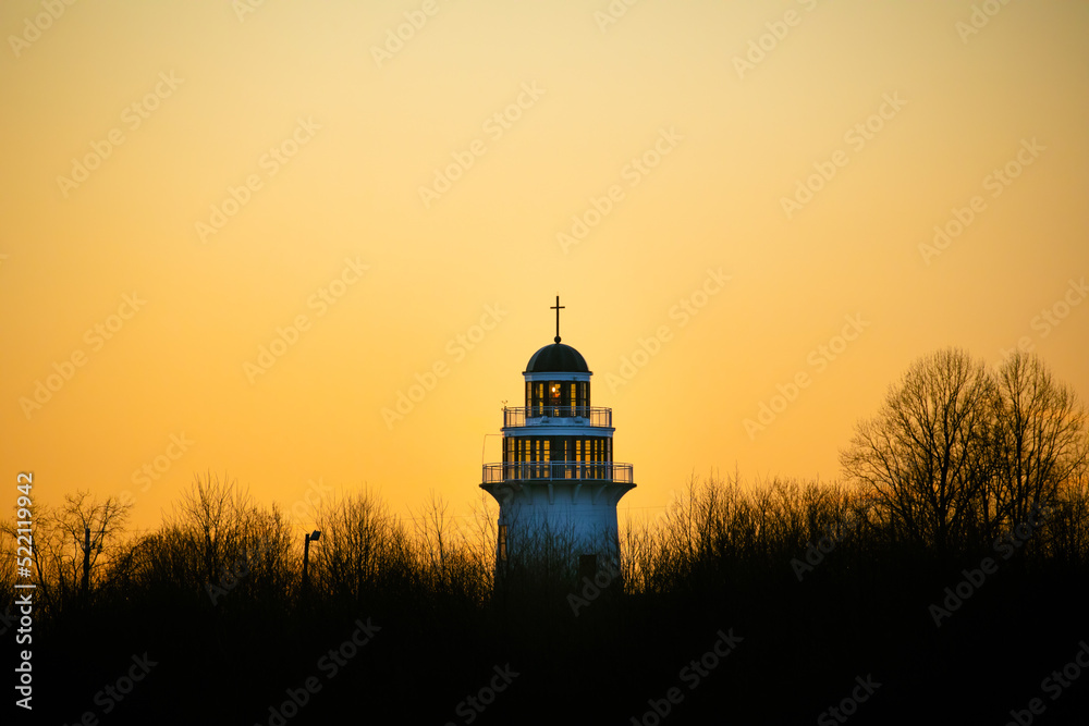Light house with a cross towering above the trees against an orange sunset in the evening