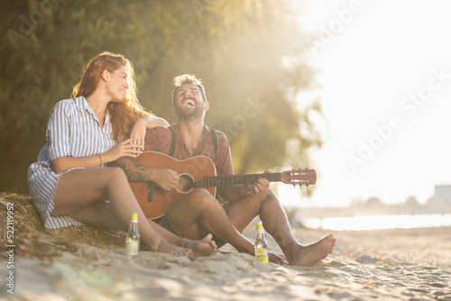 couple sitting on the beach, laughing and playing guitar